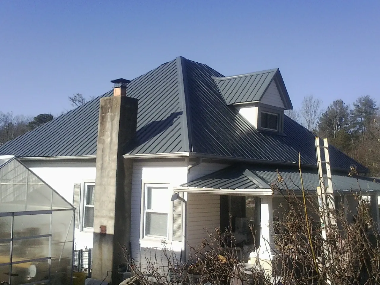 Dark blue standing seam metal roof on a white farmhouse with dormer — Slate & Tile Roof Repair by Roofing Brothers in Claiborne
