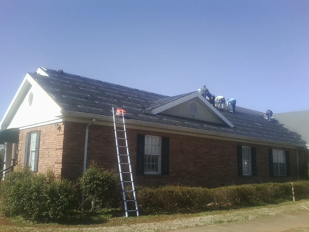 Crew tearing shingles off a brick ranch roof with a ladder set — Emergency Roof Repair work by our crew in Claiborne