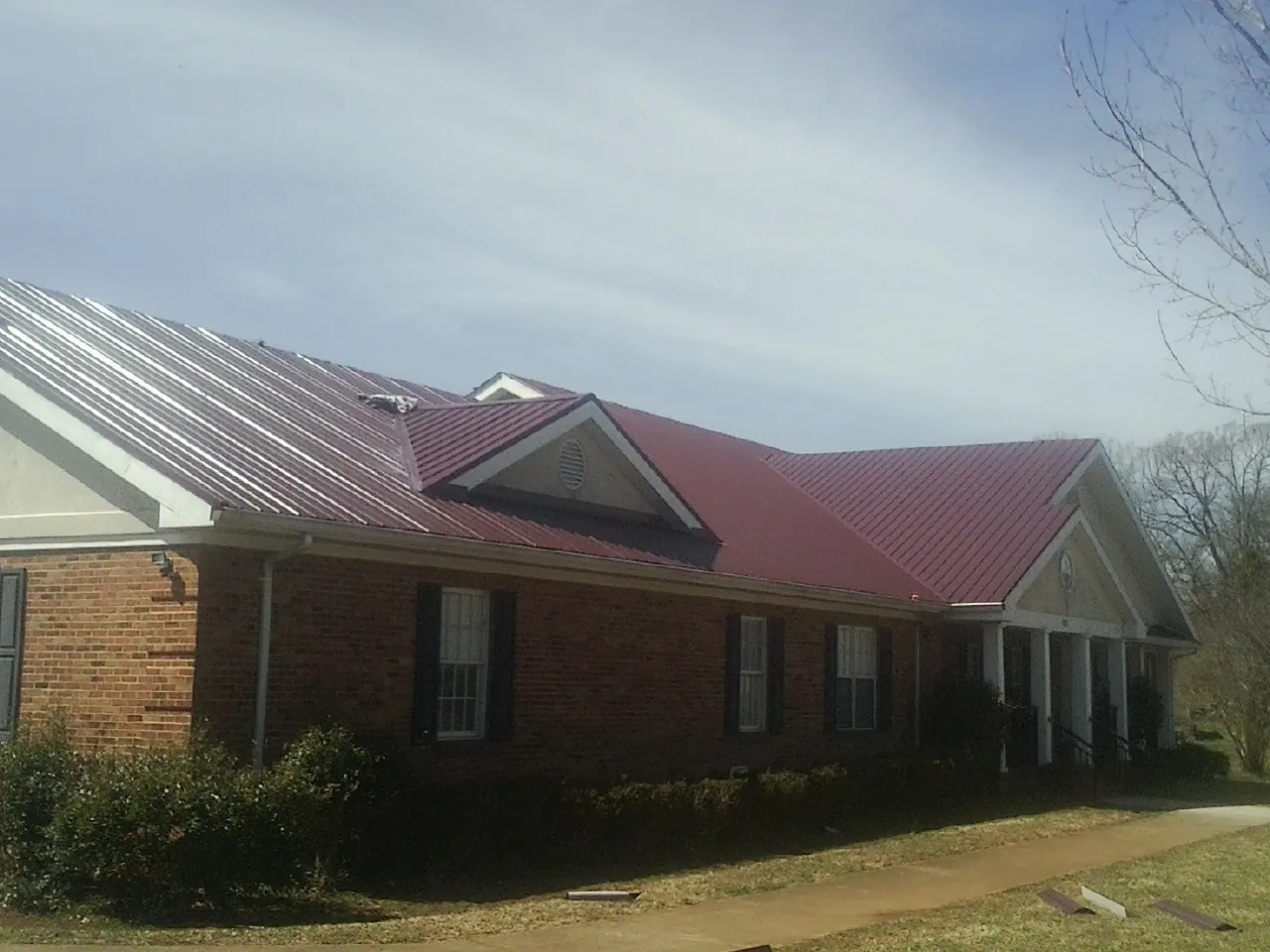 Red metal roof with gabled entries on a long brick building, from a Hail Damage Roof Repair job in Claiborne