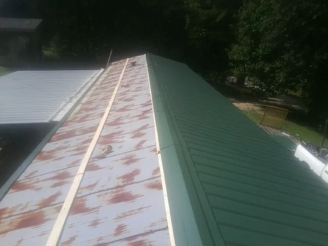 Old rusted panels beside newly installed green metal roofing — Wind Damage Roof Repair by Roofing Brothers in Claiborne
