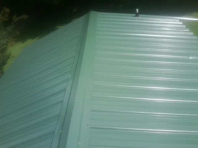 New green metal panels meeting at the ridge of a roof — Flat Roof Repair work by our crew in Claiborne