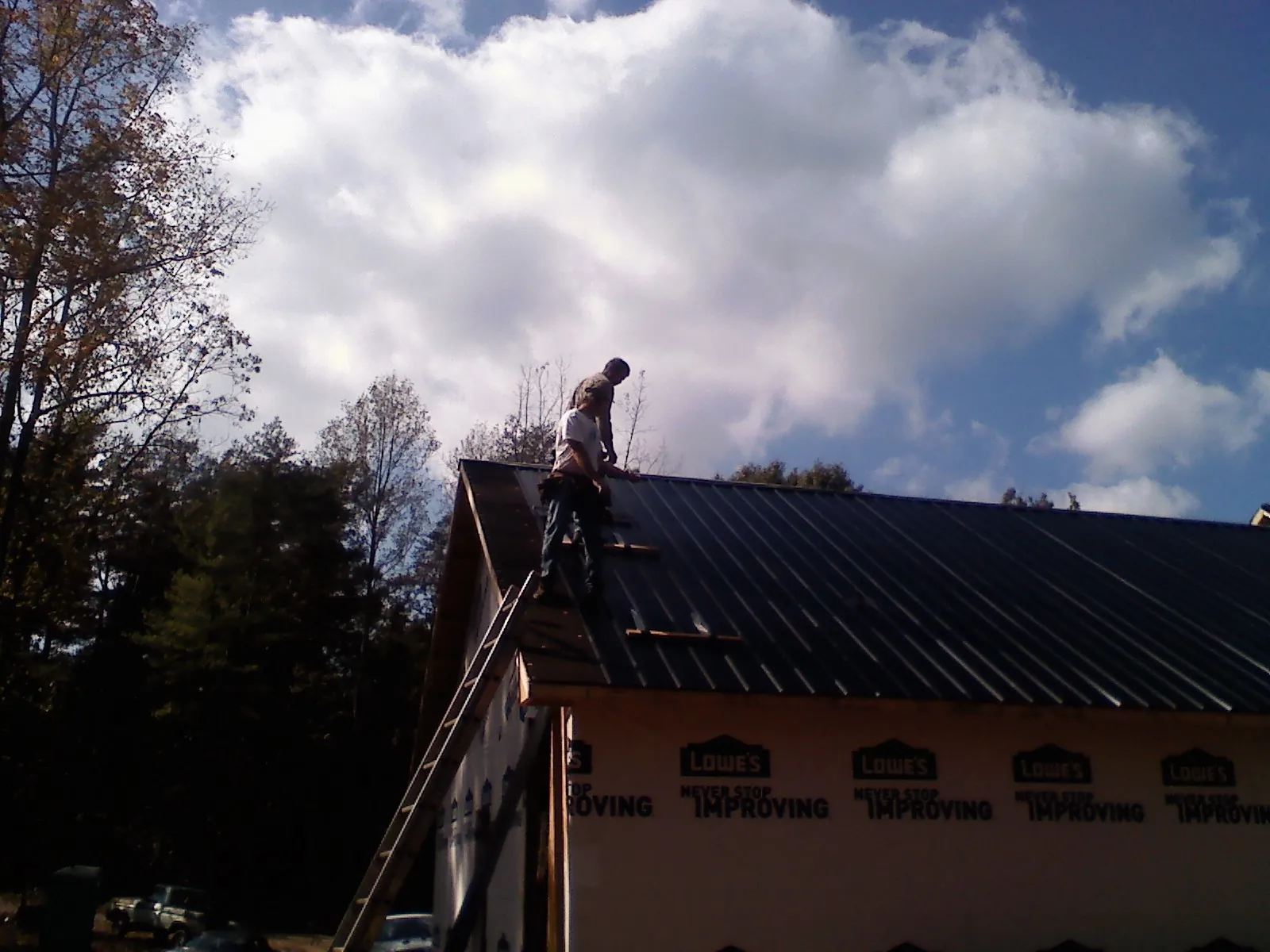 Roofer fastening dark metal panels high against a cloudy sky, from a Roof Inspection job in Claiborne