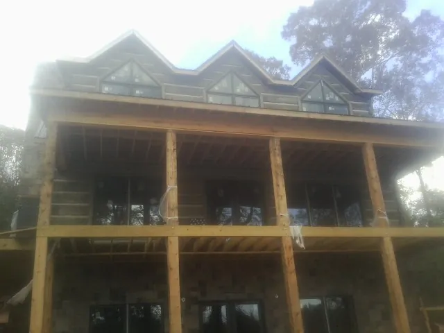 Dormers and porch framing on a large log home under construction — Roof Coating work by our crew in Claiborne