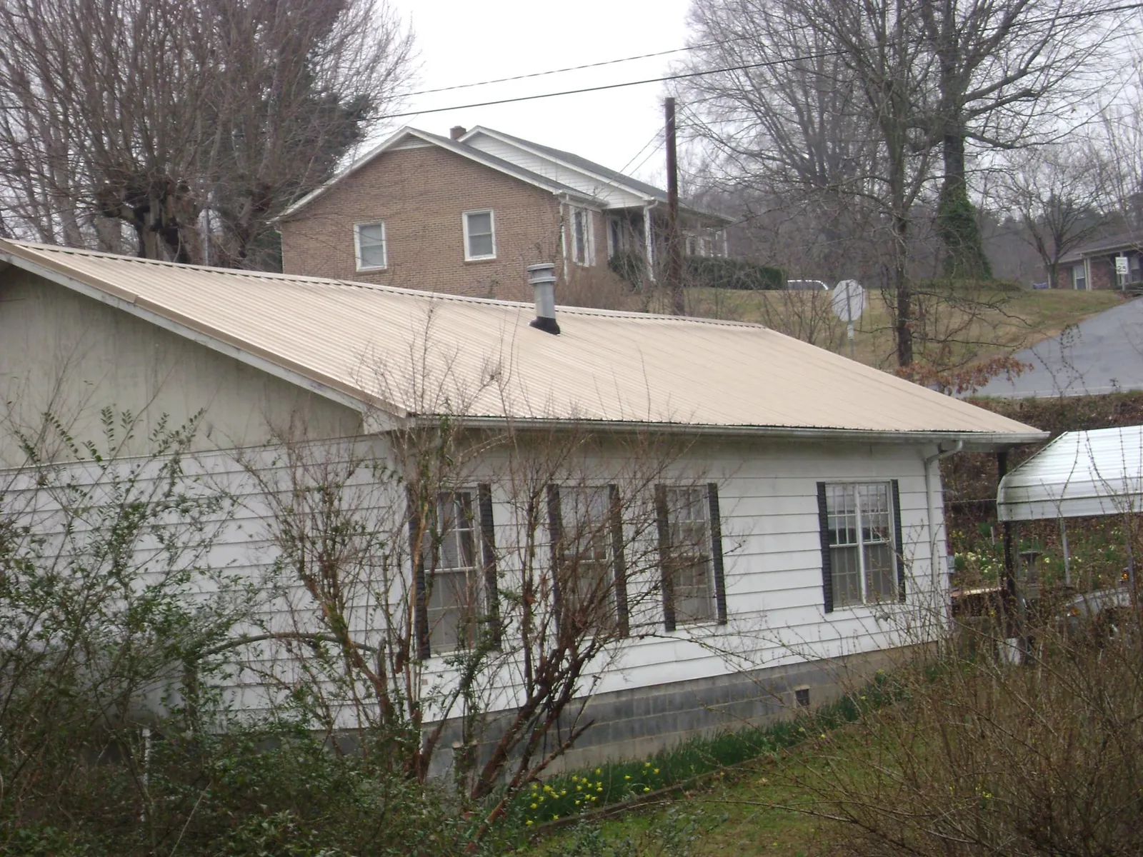 Tan metal roof on a white sided house set into a hillside — Commercial Roofing by Roofing Brothers in Claiborne
