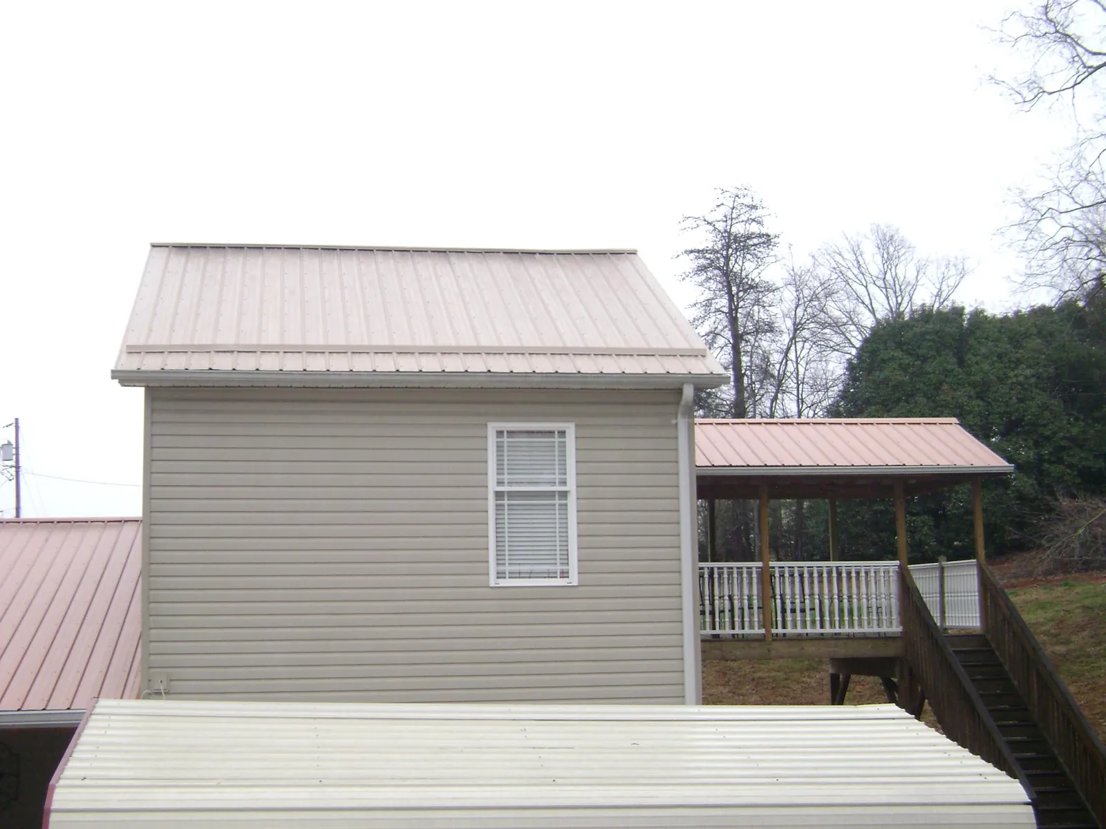 Tan metal roofs on a two story addition and attached porch, from a Roof Replacement job in Claiborne
